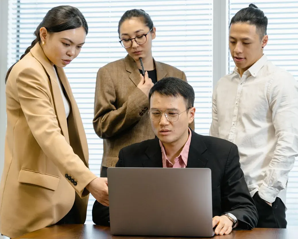 Empat orang menyimak layar laptop dalam pembahasan di ruang rapat