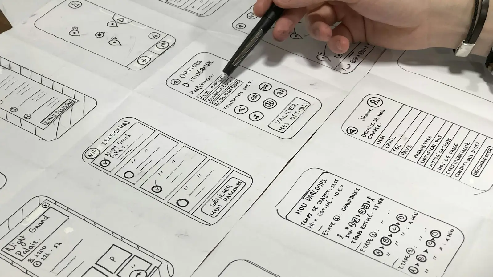 A hand pointing at sketches of mobile app screens