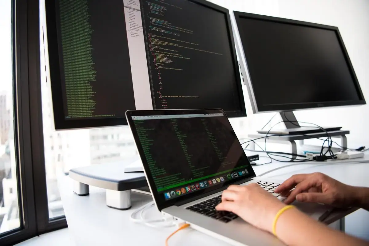 Penerapan RAD digambarkan dengan seseorang sedang coding dengan menggunakan laptop dan dua monitor PC di atasnya.