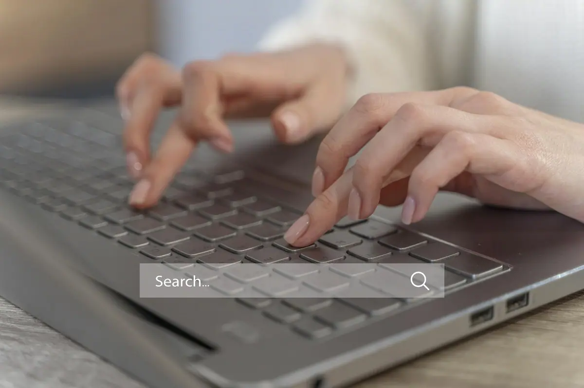 hand typing on keyboard laptop with search bar