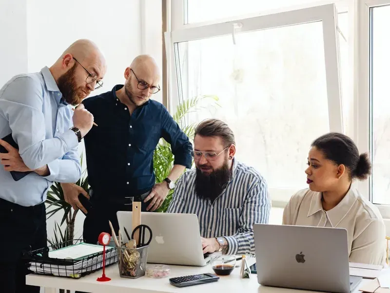 Four people reviewing work together in front of a laptop
