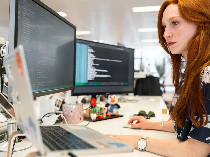 Seorang developer menulis kode di depan dua layar